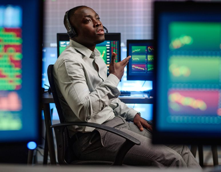Young African American man working in modern brokerage company having problems with his client trying to explain issue on phone