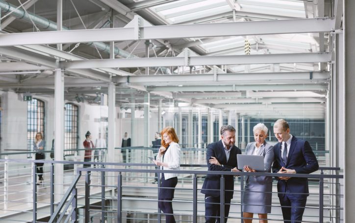 Group of businesspeople looking at project on laptop in company corridor